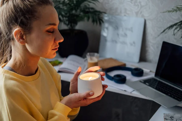 Young woman sitting on workplace at home office with lights candles, enjoy meditation, relaxing at home. Mental health, self care, No stress, mindfulness lifestyle, anxiety relief concept.