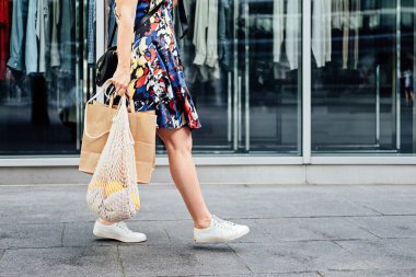 Sürdürülebilir Eko Friendly yavaş moda alışverişi. Beyaz, yeniden kullanılabilir bez çanta ve kostüm mağazası arka planında kağıt alışveriş torbası olan bir kadının yüzsüz portresi.
