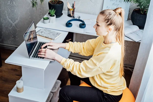 Sitting on gym ball at work. Use exercise ball like chair at workplace. Freelancer woman sitting on orange fitness ball using laptop in home office.