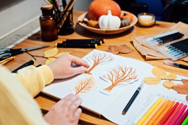 Yetişkinler için sonbahar sanatı. Sonbahar sanat yaratıcı kolajı. Kalemlerle sonbahar ağaçları çizen ve kağıttan kolaj kesen kadının yüzsüz portresi.