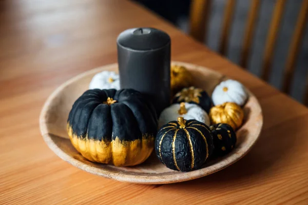 Decorating Pumpkins ideas. Trending painting Black Gold White Pumpkin in round plate. Minimal Top view flat lay autumn composition with painting black golden trendy pumpkins.