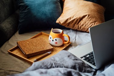 Sıcak bir ev, sonbahar sıcağı. Dizüstü bilgisayar, defter ve çay tepsisi yatak odasındaki battaniyenin üzerinde. Sıcak sonbahar ya da kış konsepti