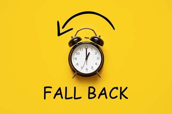 Daylight saving day. Fall Back. Black Alarm clock and autumn leaves and text Fall Back on yellow background. Daylight saving time end.
