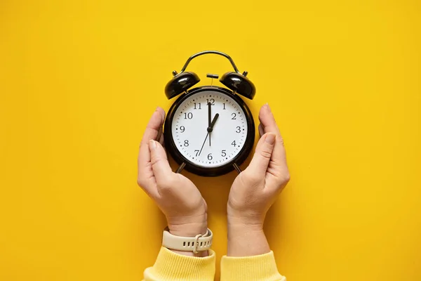 Daylight saving day. Fall Back. Black Alarm clock and female hands on yellow background. Daylight saving time end.