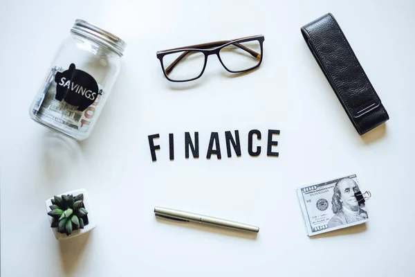 Finance Courses Online. Budget Planner. Word Finance, laptop, mason jar saving bank, stationery and glasses on table.