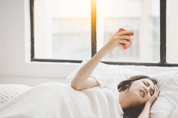 Young beautiful asian woman hate waking up early in the morning Young woman pressing snooze button on early morning alarm clock Headache girl stopping alarm clock on her bed in early morning on Monday