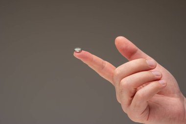Kafkas erkeğinin işaret parmağında çok küçük bir L1131 pil hücresi var. Yakın çekim, gri arkaplanda izole edilmiş..