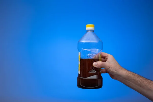 用透明的塑料瓶回收用过的食用油 被男人牵着手特写镜头 蓝色背景隔离 — 图库照片