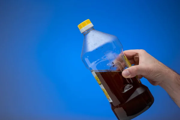 用透明的塑料瓶回收用过的食用油 被男人牵着手特写镜头 蓝色背景隔离 — 图库照片