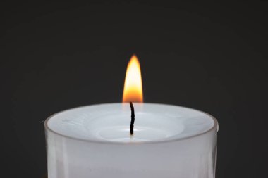 Küçük beyaz bir mum yanıyor. Stüdyo çekimini kapat, karanlık arka planda izole edilmiş..