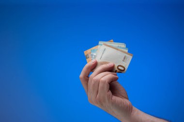 Avrupa para birimi banknotları erkek eliyle tutulur. Stüdyo çekimini kapat, mavi arkaplanda izole edilmiş..