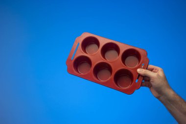 Beyaz erkek eli kesikli boş kırmızı seramik kek tepsisi. Stüdyo çekimini kapat, mavi arkaplanda izole edilmiş..