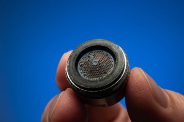 Old dirty limescale covered clogged up tap water faucet strainer or aerator held in hand by Caucasian male. Close up studio shot, isolated on blue background. clipart