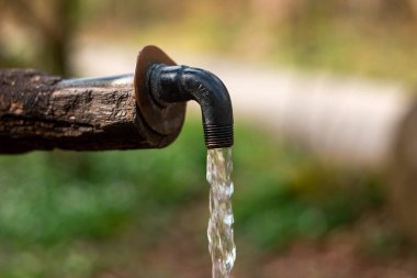 Tahta ve metal musluktan yapılmış su fıskiyesi. Akan temiz su, yakın çekim, sığ alan derinliği, orman manzarası, insan yok..