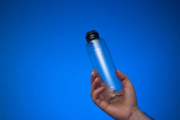 白人男性の手で手に持ってキャップで空の透明なプラスチック製の水ボトル スタジオショットを閉じて 青の背景に隔離された — ストック写真