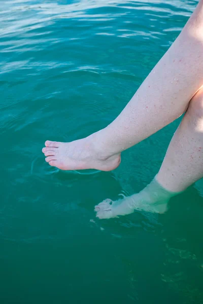 Unrecognizable caucasian woman dipping her bare feet in clean and clear lake water. Sunny summer day