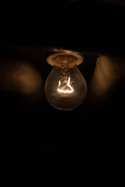 Very dim incandescent light bulb mounted on a cellar ceiling. Close up shot, no people, glowing filament.