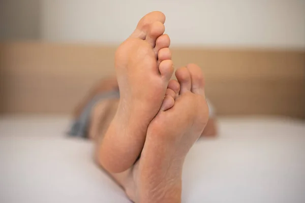 Caucasian man's bare feet laying on a bed, shallow depth of field, unrecognizable face.