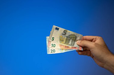 20, 10 ve 5 avroluk banknotlar, beyaz bir erkek tarafından elde tutuluyor. Stüdyo çekimini kapat, mavi arkaplanda izole edilmiş..