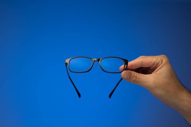 Siyah plastik gözlük, beyaz bir erkeğin elinde duruyor. Stüdyo çekimini kapat, mavi arkaplanda izole edilmiş..