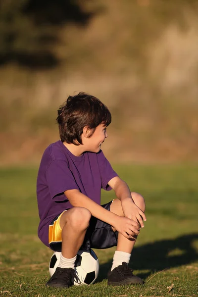 Menino sentado na bola de futebol — Fotografia de Stock