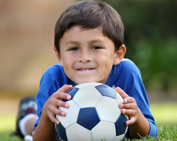 Молодий іспаномовний хлопчик лежить з футбольним м'ячем Стокове Фото