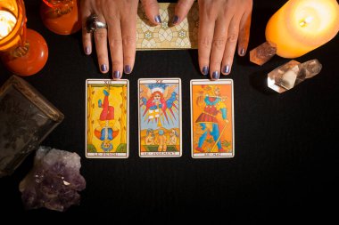 Siyah kart masasında duran üç tarot kartını gösteren bir kadının elleri. Tarot kartlarıyla kehanet oturumu. Yukarıdan görüntüle.