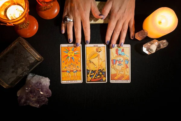 Siyah kart masasında duran üç tarot kartını gösteren bir kadının elleri. Tarot kartlarıyla kehanet oturumu. Yukarıdan görüntüle.