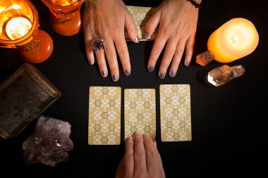 Bir kadının üç tarot kartını siyah kart masasının üstünde gösterirken diğer elin kartlardan birini tutmasının ayrıntıları. Tarot kartlarıyla kehanet oturumu. Yukarıdan görüntüle.