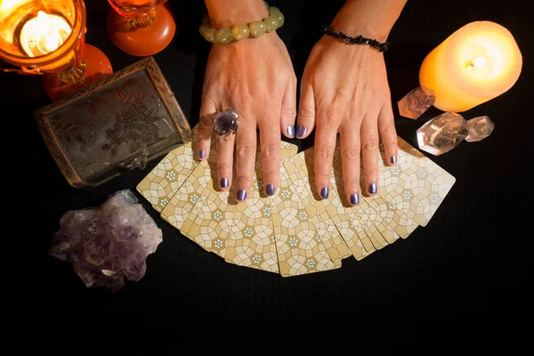 Detail of a woman\'s hands on tarot cards on a black card table. Concept of a fortune telling session with tarot cards.