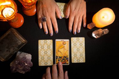 Bir kadının elinde siyah kartlardan oluşan bir masada üç tarot kartı gösterirken, diğer elinde seçilmiş kişi olarak ölüm kartı görülüyor. Tarot kartlı kehanet oturumu. Yukarıdan görüntüle.
