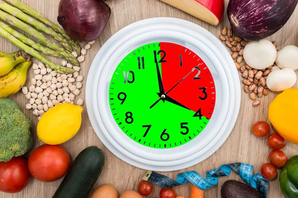 時計は 健康的な食べ物に囲まれ 1つの部分は赤でマークされ 1つは緑です 間欠的断食の概念 オートファジーの再生メカニズムなどの利点を提供する食事 — ストック写真