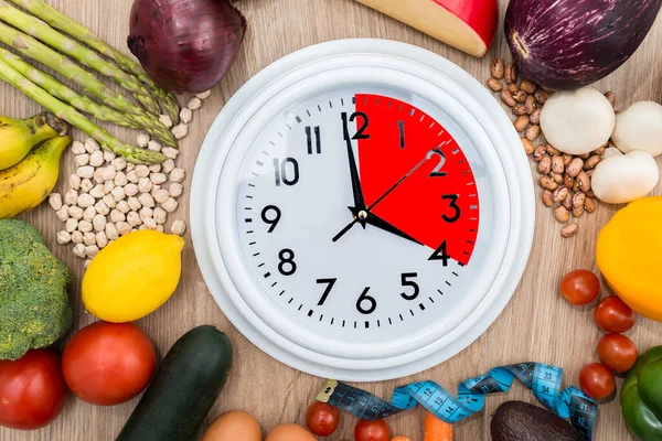 時計は 健康的な食べ物に囲まれ 部分的に赤でマークされます 間欠的断食の概念 オートファジーの再生メカニズムなどの利点を提供する食事 — ストック写真