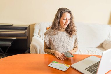 Akıllı telefonlu ve dizüstü bilgisayarın önünde Covid19 antijen testleri hakkında internetten bilgi arayan bir kadın..