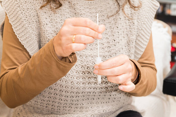 Detail of a woman's hands preparing a sample for a covid19 antigen self-test in her living room.