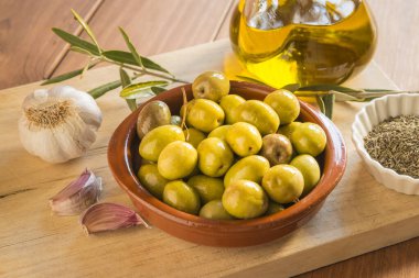 Bir kase zeytinle sakin bir hayat, farklı baharatlarla süslenmiş, ahşap bir tahtada. Ev yapımı zeytin, geleneksel Akdeniz mutfağı..