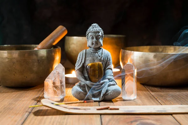 Still life with Tibetan bowls, minerals, candles and a Buddha figure on wooden boards and a dark background. Small altar illuminated with small candles for meditation and music therapy.