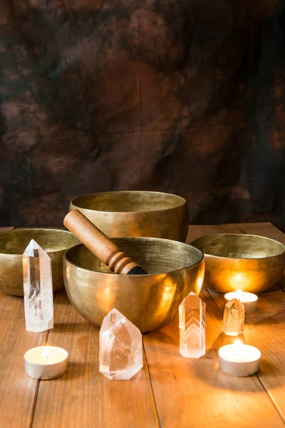 Still life with Tibetan singing bowls, minerals and candles on wooden boards and a dark background with copy space. Small altar illuminated with small candles for meditation and music therapy.