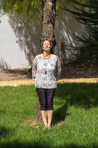 A woman sunbathes standing and hugging a tree. Hugging a tree has many health benefits.