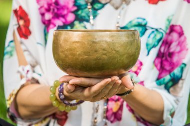 Bir park alanında meditasyon ve müzik terapisi sırasında Tibet şarkı kasesi tutan bir kadının ellerinin ayrıntıları.