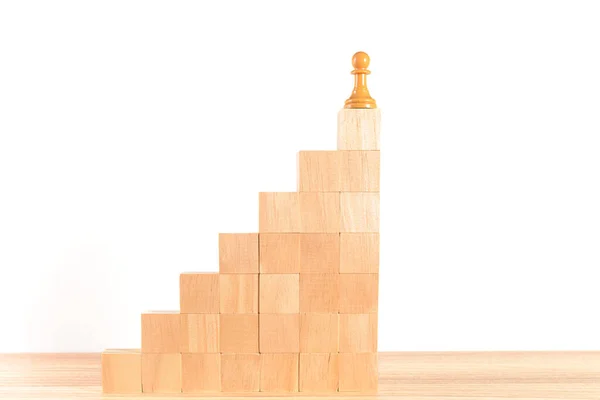 Chess pawn at the top of a staircase made of wooden blocks, with a white background. Concept of self-improvement, leadership and success. Space for copying.