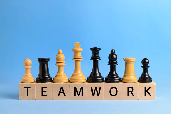 White and black chess pieces on wooden blocks with the word teamwork written on them, on a blue background. Concept of teamwork and cooperation.