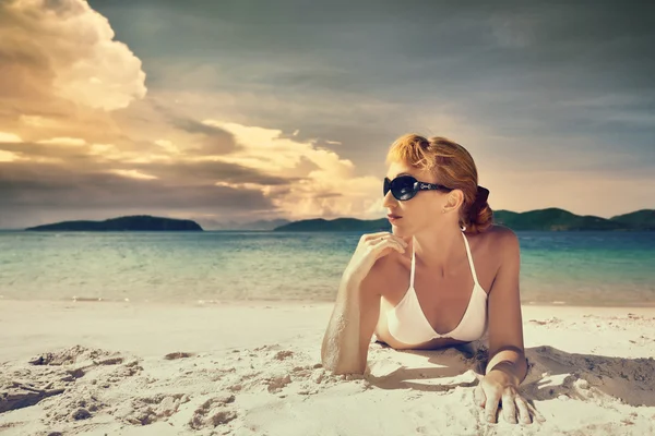 Una mujer guapa en bikini tomando el sol en la playa sobre un fondo — Foto de Stock