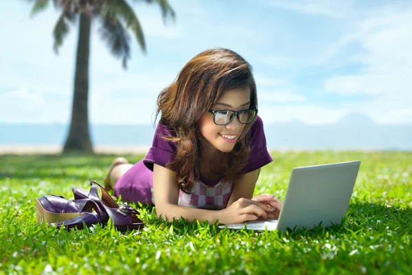 Pretty Asian girl is resting under the palm trees on the grass w — Stock Photo, Image