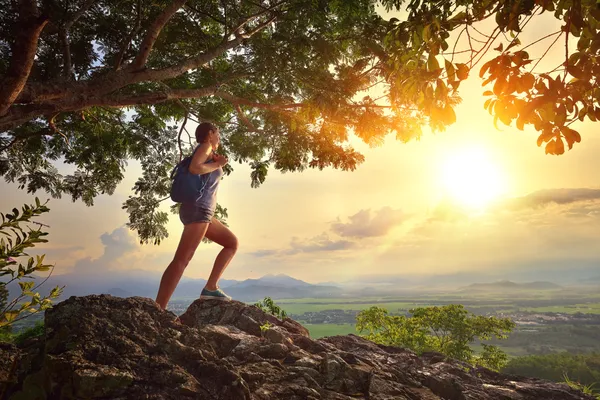 Young woman admires the sunset with a backpack standing on cliff — Stock Photo, Image