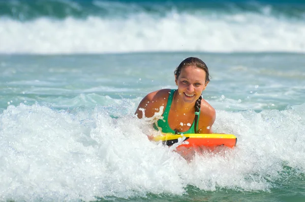 Joven mujer atractiva bodyboards en tabla de surf con una sonrisa agradable —  Fotos de Stock