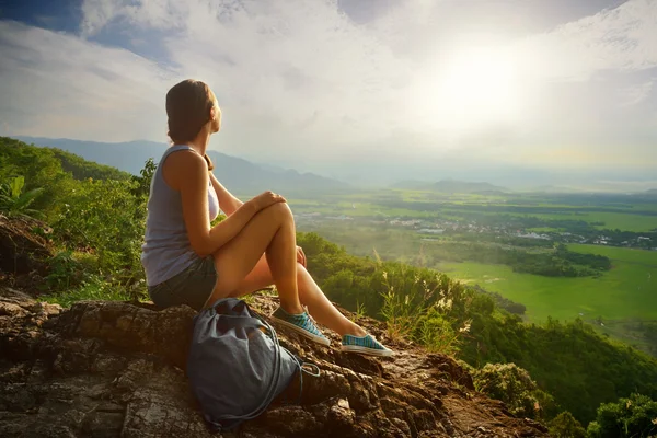 Bir kız uçurumun kenarında oturur ve güneş vadisine ve dağlara bakar. — Stok fotoğraf