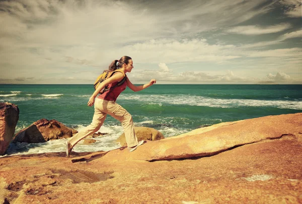 Jovem com uma mochila corre em rochas costeiras — Fotografia de Stock