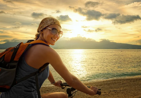 Mujer joven con mochila de pie en la orilla cerca de su bicicleta un —  Fotos de Stock