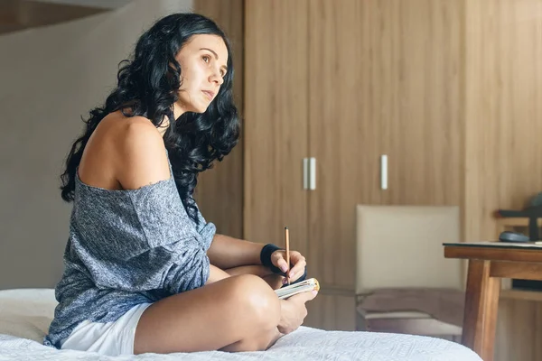 Young pensive woman artist draws with a pencil in notebook Stock Photo